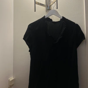 Svart blus från Cappuccino! - Säljer denna svarta blusen från Cappuccino! Säljer då den inte har kommit till användning. Blusen har en V-ringning med volanger!!! Kontakta för fler bilder! Pris kan diskuteras 