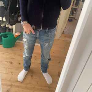 replay jeans med slitningar - Säljer ett par blå replay jeans med slitningar och en avslappnad look. De har en normal passform och är perfekta för en casual stil. Jeansen har en dragkedja och knappar framtill. Är 183 om ni vill gemföra dm för fler bilder eller funderingar. Mvh Kian 🍾🔥