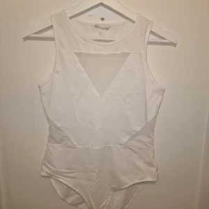 Vit bodysuit från H&M - Säljer en vit body med meshdetaljer framtill och på sidorna som ger en snygg look. Perfekt för att matcha med olika outfits. Använd vid 1 tillfälle. Garderobsrensning så kika gärna på övriga auktioner.