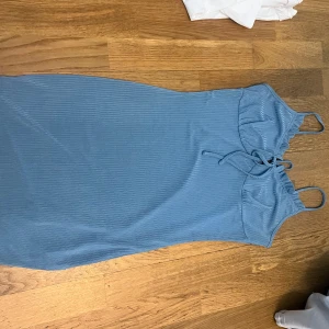 Blå ribbad klänning - Snygg blå ribbad klänning med smala axelband och knytning framtill. Perfekt för en somrig look. Klänningen har en figurnära passform och är tillverkad i ett mjukt material som ger en bekväm känsla.