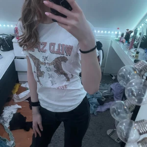 Vit t-shirt med tigertryck från Ginatricot - Säljer en vit t-shirt med trycket 'Wild Spirit' och två tigrar på framsidan. Texten 'Seoul 89' finns också med. Perfekt för en avslappnad stil.