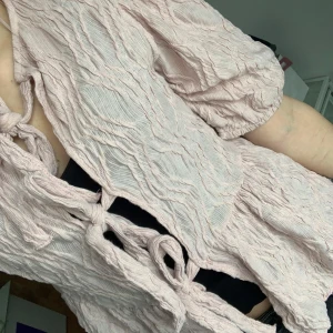 Ljusrosa blus från Gina Tricot - Säljer en söt ljusrosa blus från Gina Tricot i storlek XS. Blusen har korta ärmar och ett knytband framtill. Materialet är lätt och luftigt med en krinklad textur. Perfekt för en avslappnad och stilren look.💞
