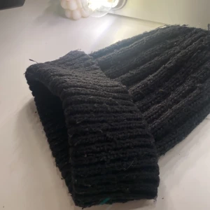 Svart stickad mössa - Säljer en svart stickad mössa med ribbad design. Perfekt för kyliga dagar och ger en stilren look. Mössan är mjuk och bekväm att bära. Nopprig men annars bra skick 