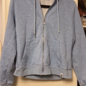 Ljusblå zipup hoodie - Mysig ljusblå hoodie från FB Sister med dragkedja och justerbar huva. Perfekt för en avslappnad stil. Den har praktiska fickor framtill och ribbade muddar vid ärmslut och nederkant.