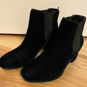 Blå boots från H&M - Snygga blå boots från H&M i sammet med en bekväm klack. De har en klassisk chelsea boots-design med elastiska paneler på sidorna för enkel på- och avtagning. Perfekta för att ge en stilren touch till din outfit. Nyskick 