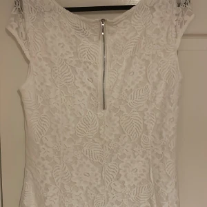 Vit student spetsklänning med dragkedja -  vit spetsklänning med vackert blommönster. Klänningen har en dragkedja i ryggen och korta ärmar. Perfekt för sommaren eller studenten 🌸🌸 Storlek M 