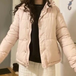 Ljusrosa pufferjacka - Säljer en ljusrosa pufferjacka med dragkedja och knappar. Jackan har långa ärmar och en mysig, quiltad design som passar perfekt för kyligare dagar.