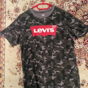 Camouflage t-shirt från Levi's - Snygg camouflage t-shirt från Levi's med det klassiska röda logotyptrycket på bröstet. Perfekt för en avslappnad stil. Kortärmad och i en cool grön och grå färgkombination. Militär grön färg som är unik