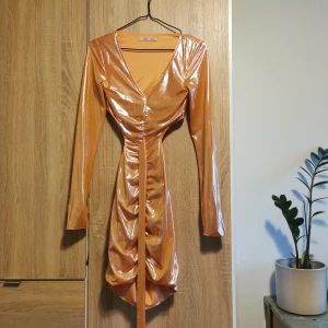 (XS/6) Glansig orange klänning från Jaded Rose - Snygg glansig orange klänning från Jaded Rose i polyester. Ger mig lite "winx Club" - vibes. Storlek 6 / XS / 32/34. Öppen rygg och med snöre som knyts bak (eller fram om man vill). 