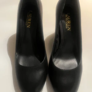 Svarta pumps från Lauren Ralph Lauren - Eleganta svarta pumps från Lauren Ralph Lauren i skinn. Skorna har en klassisk design med rund tå och en stabil klack. Perfekta för en stilren look.