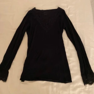 Svart långärmad topp från Intimissimi - Elegant svart långärmad topp från Intimissimi med vacker spetsdetalj vid halsringningen och ärmsluten.  Sällan använd och är i bra kvalitet