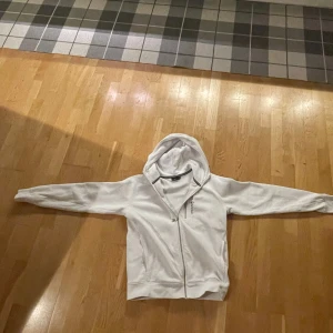 Vit hoodie från Sail Racing - Säljer en stilren vit hoodie från Sail Racing. Den har en dragkedja framtill och en bekväm huva. Perfekt för en avslappnad stil. Helt ny, hör av er vid minsta lilla fundering, priset sitter inte i sten😀