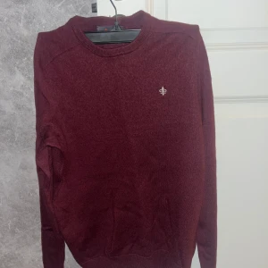 Vinröd tröja från Morris - Säljer en stilren vinröd tröja från Morris i 100% merinoull. Tröjan har en liten broderad logga på bröstet och rund halsringning. Perfekt för kyligare dagar. Tröjan är som ny utan några som helst hål eller defekter.