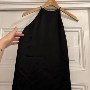 Svart axelbandslös topp - Elegant svart axelbandslös tppp med en stilren design. Perfekt för festliga tillfällen. Toppen har en enkel och tidlös stil som gör den lätt att matcha med olika accessoarer.