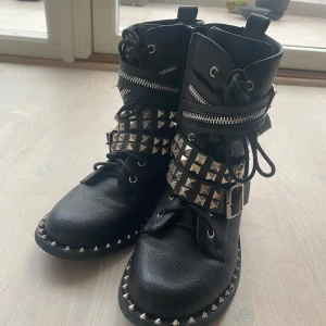 Svarta boots med nitar från Lu Boo - Snygga svarta boots från Lu Boo med coola nitar och spännen. Skorna har både snörning och dragkedja. Perfekta för att ge din outfit en tuff touch.
