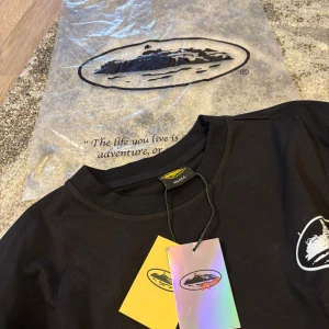 Svart t-shirt från Nike och Corteiz - Snygg svart t-shirt från Nike med tryck på både fram- och baksidan. Framsidan har en vit Nike-logga och ett ovalt märke, medan baksidan har texten 'DUN IT.' i stora vita bokstäver. Perfekt för en casual look.