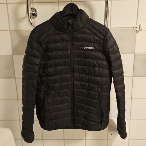 Svart pufferjacka från Stormberg - Säljer en svart pufferjacka från Stormberg. Jackan är perfekt för kyligare dagar med sitt quiltade mönster och långa ärmar. Den har en dragkedja framtill och är i nyskick. Superbra för både höst och vinter!