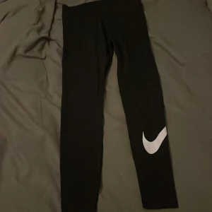 Svarta leggings från Nike - Säljer ett par svarta leggings från Nike i storlek M. De är i bra skick och har den klassiska Nike-loggan i vitt på benet. Perfekta för träning eller en avslappnad dag. Superbekväma och stretchiga!