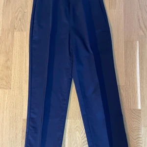 Mörkblå byxor från M&S Collection - Säljer ett par eleganta mörkblå byxor från M&S Collection. De är i storlek EUR 34 och har en klassisk rak passform. Perfekta för både vardag och festliga tillfällen. Byxorna är i nyskick och har en stilren design som passar till det mesta.