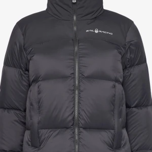 Svart dunjacka från Sail Racing - Säljer en snygg och varm svart dunjacka från Sail Racing. Jackan har en hög krage och dragkedja framtill. Perfekt för kalla vinterdagar. Den är i nyskick och har en stilren design med logotypen på bröstet och ryggen. Storlek är oklart. 