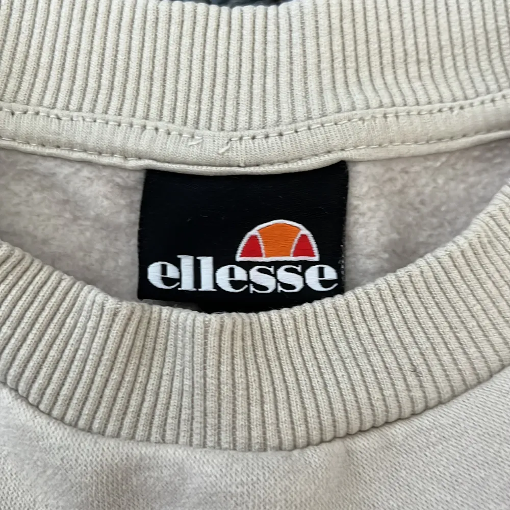 Säljer en snygg beige sweatshirt från Ellesse i storlek S. Tröjan har en klassisk design med ribbade muddar och en liten broderad logga på bröstet. Perfekt för en avslappnad stil och passar till alla årstider. Skön och stilren, ett måste i garderoben!. Tröjor & Koftor.