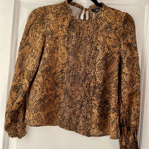 Mönstrad blus från Zara - Säljer en superfin blus från Zara. Den har ett coolt ormmönster i bruna och svarta toner. Blusen är långärmad och har en liten knytning vid nacken. Står storlek S men upplever att den är en XS. I mycket bra skick!