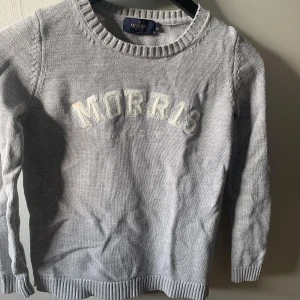 Grå stickad tröja från Morris - Säljer en snygg och stilren grå stickad tröja från Morris. Den har ett broderat Morris-märke på framsidan och är i storlek XS. Perfekt för höst och vinter med sina långa ärmar och ribbade kanter. Supermysig och passar till allt! en liten fläck vid M