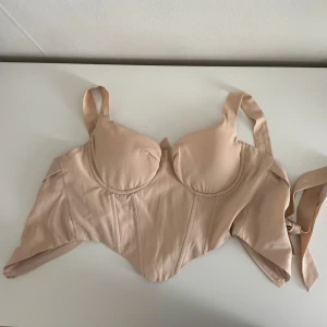 Beige korsett i polyester - Säljer en snygg beige/puderrosa korsett/topp i storlek XS. Den är gjord av 95% polyester och 5% elastan, vilket gör den stretchig och bekväm. Korsetten har en dragkedja bak och breda axelband för extra stöd. Perfekt för en festlig kväll eller som en stilren detalj under en kavaj.