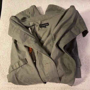 Grön jacka från Clara & Co - Säljer en snygg grön jacka från Clara & Co. Jackan har en normal passform med långa ärmar och praktiska fickor. Perfekt för vår och höst! Den har både knappar och dragkedja för stängning. Superbra skick och redo för nya äventyr!