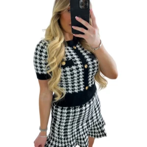 Co-ord set kjol och topp XS - Snygg tvådelad set i svart och vitt rutmönster med guldfärgade knappar. Toppen har korta ärmar och en rund halsringning. Kjolen är en A-linje med volanger i nederkanten.  Settet är oandvänt. 