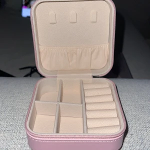 Rosa smyckeskrin med dragkedja - Praktiskt och stilrent rosa smyckeskrin med dragkedja. Perfekt för att organisera dina smycken med flera fack och hållare för ringar. Kompakt design som är lätt att ta med på resor.