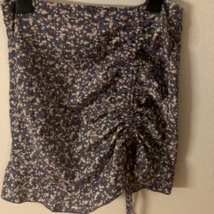 Blommig kjol från Shein - Söt blommig kjol från Shein i blått med små vita och rosa blommor. Kjolen har en rynkad detalj framtill och en knytning som ger en fin passform. Perfekt för sommaren!