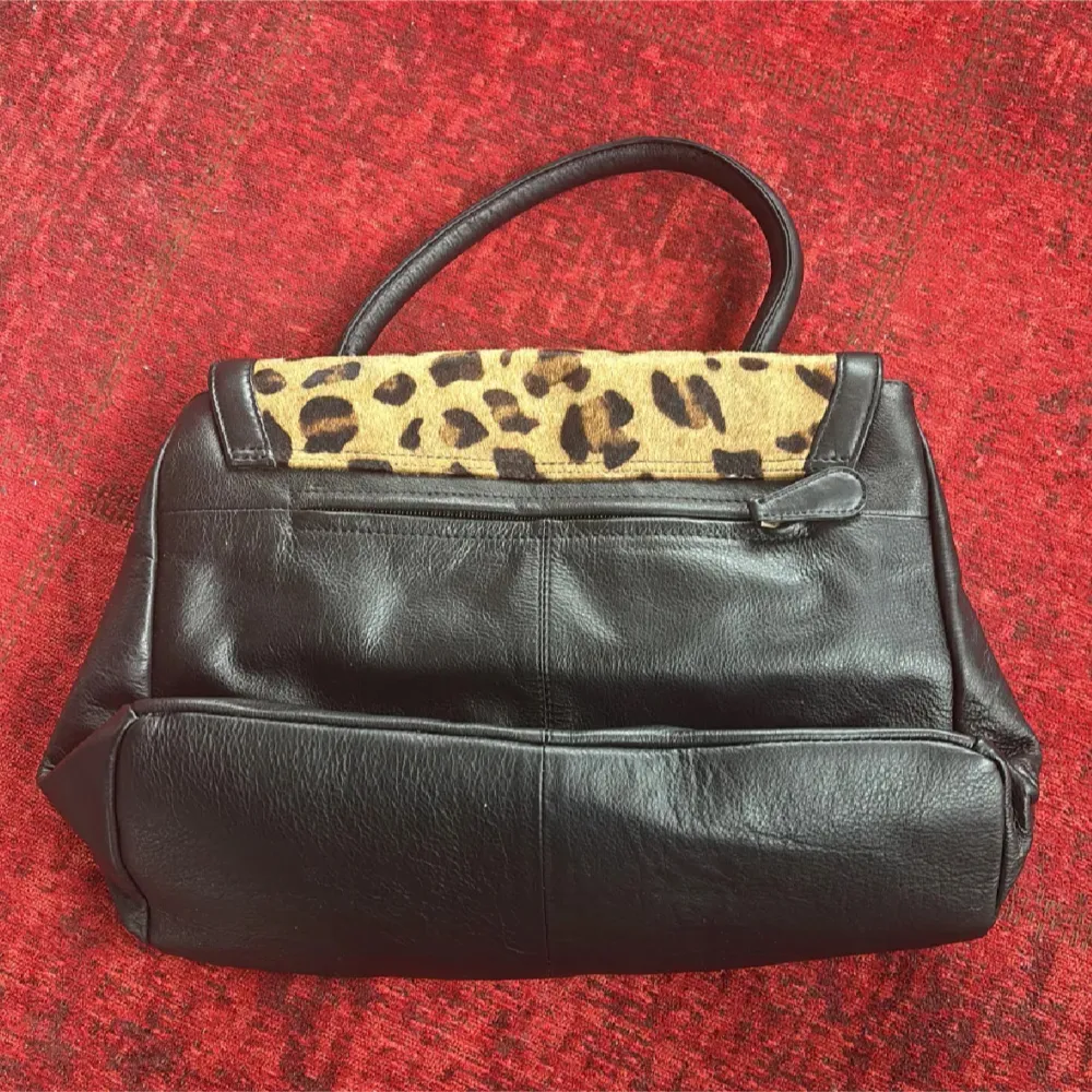 Snygg svart handväska i skinn med leopardmönstrad framsida. Väskan har ett praktiskt handtag och ett elegant spänne framtill. Perfekt för att ge din outfit en djärv touch. Helt ny❤️. Laukut & Käsilaukut.