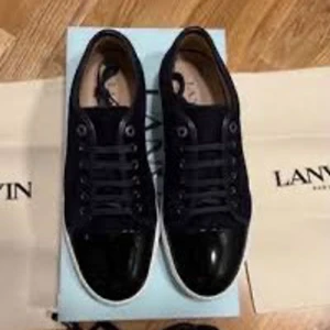 Svarta sneakers från Lanvin - Snygga svarta sneakers från Lanvin med glansig tå och klassisk snörning. Perfekta för en stilren look med en touch av elegans. Skorna har en vit sula som kontrasterar snyggt mot det svarta.
