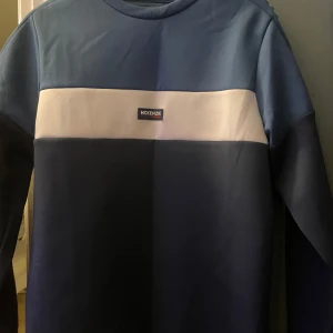 Blå tröja från McKenzie - Snygg blå tröja från McKenzie med en vit panel över bröstet och broderad logga på axeln. Tröjan har långa ärmar och en rund halsringning. Perfekt för en stilren och avslappnad look. Har ett stretchigt tyg med så den är väldigt skön 