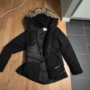 Svart Fjällräven parkajacka med päls - Säljer en svart parkajacka i toppskick med pälsdetaljer på huvan. Jackan säljs då jag har för många jackor. Jackan har en dragkedja framtill och är långärmad. Perfekt för kyliga dagar med sin varma och skyddande design. Nypris är 6000kr. Pris kan diskuteras vid snabb affär