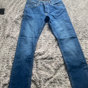 Blå jeans från Jack & Jones slim  - Snygga blå jeans från Jack & Jones i slim fit. Perfekta för en stilren look med klassisk femficksdesign och knappgylf. Passar utmärkt till både vardag och mer uppklädda tillfällen.