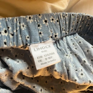 Blå blommig kjol från Lindex - Söt blå kjol från Lindex med små vita blommor och volangdetaljer. Perfekt för en lekfull och somrig look. Resår i midjan för extra komfort.