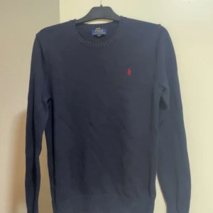 Mörkblå tröja från Ralph Lauren - Snygg mörkblå tröja från Ralph Lauren med det klassiska röda broderade logotypen på bröstet. Tröjan har en rund halsringning och är tillverkad i ett mjukt material som ger en bekväm passform. Perfekt för en stilren look. Den är äkta, skick 8/10 frågor? DM!