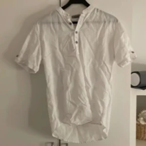 Vit kortärmad skjorta från Reverb - Säljer en stilren vit kortärmad skjorta från Reverb. Skjortan har en enkel design med knappar framtill och en ståkrage. Perfekt för en avslappnad och snygg look.