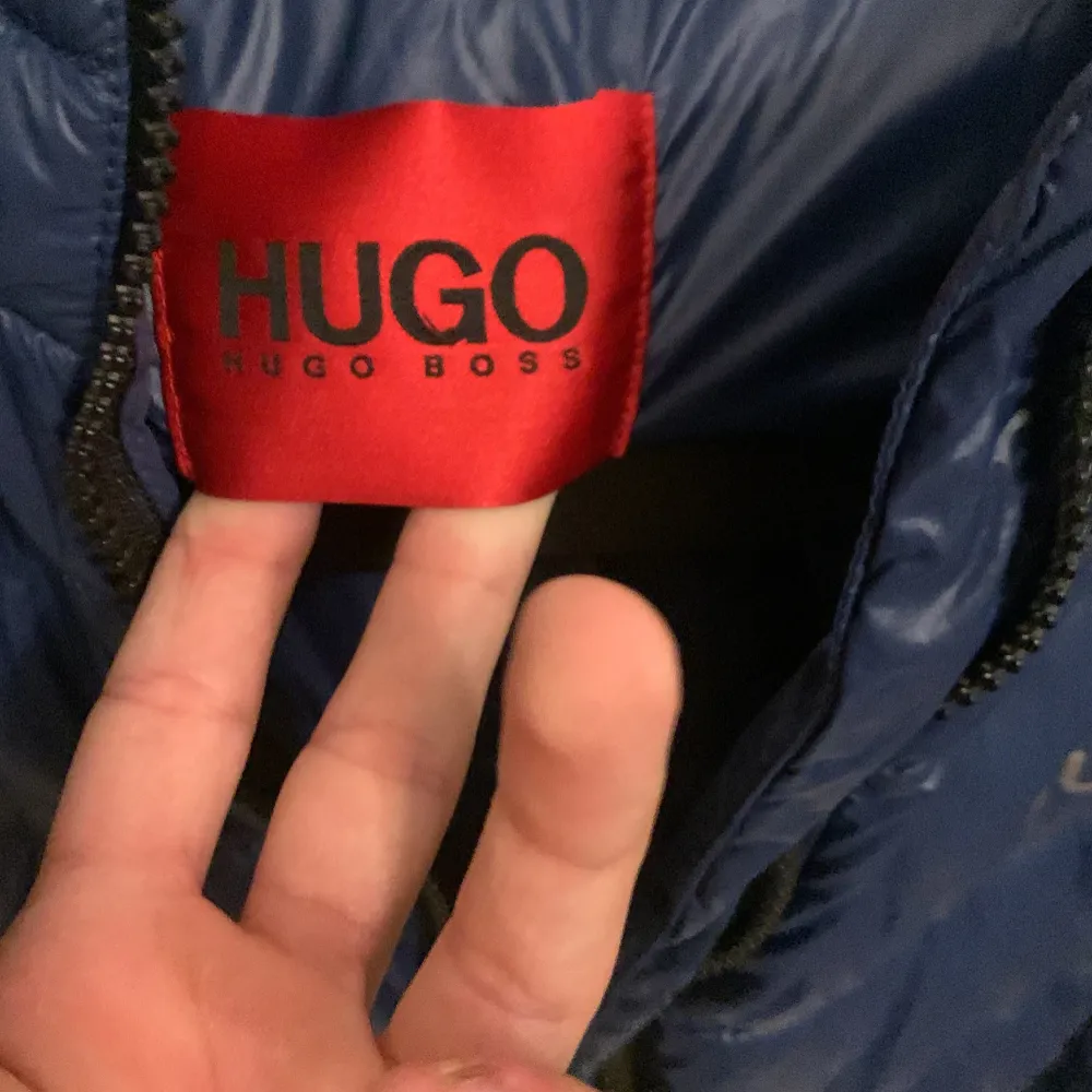 Säljer en snygg blå dunjacka från Hugo Boss. Jackan har en quiltad design med dragkedja framtill och en praktisk huva. Perfekt för kyligare dagar och ger en stilren look. Passar både till vardags och mer uppklädda tillfällen.. Takit.