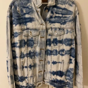 Blå- och vitmönstrad jeansjacka - Snygg jeansjacka med blå- och vitmönster i en cool, tvättad stil. Jackan har knappar framtill och två bröstfickor med knappstängning. Perfekt för en avslappnad look.