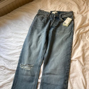 Blå 90-talsinspirerade jeans från H&M - Snygga blå jeans från H&M med en 90-talsinspirerad rak passform och hög midja. De har en cool slitning på ena benet och är tillverkade i återvunnen bomull. Perfekta för en avslappnad stil. Aldrig använda bara testade🫶🏼 NYPRS-400kr