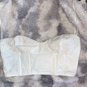 Vit broderad korsett från H&M - Säljer en söt vit korsett från H&M med broderade blommor och smala axelband. Perfekt för sommardagar. Den har en elastisk rygg för bättre passform. 
