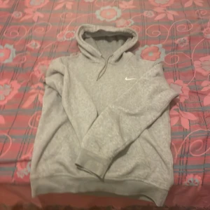 Grå hoodie från Nike - Säljer en klassisk grå hoodie från Nike med en liten vit logga på bröstet. Tröjan har en bekväm passform med långa ärmar och en praktisk huva med dragsko. Perfekt för en avslappnad stil. Hör av dig vid intresse! 😊