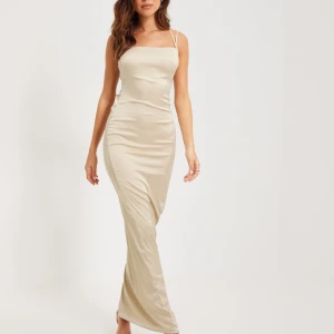 Champagnefärgad balklänning med snörning - Elegant champagnefärgad balklänning från Nelly  med smala axelband och korsad snörning i ryggen. Klänningen har en figurnära passform och är tillverkad i ett glansigt material som ger en lyxig känsla använd en gång🫶🏻