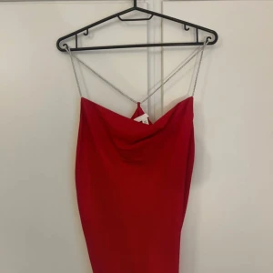 Röd topp med glittriga band  - Snygg röd topp med tunna kedjeband som ger en elegant touch. Toppen har en draperad design framtill och är perfekt för en kväll ute. Den är snygg och har en smickrande passform. Aldrig använd 