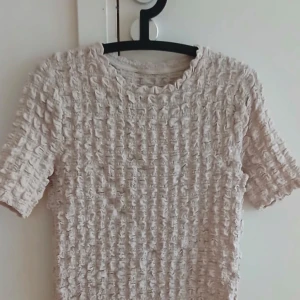 Beige ribbad topp - Säljer en beige ribbad topp med korta ärmar. Perfekt för en stilren och bekväm look. Passar bra till både jeans och kjol. Hör av dig vid intresse! Jättefin ! Knappast  andvänd 