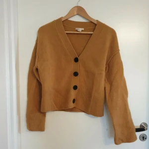 Brun kofta i ullblandning - Säljer en mysig brun kofta i ullblandning med stora svarta knappar framtill. Koftan har en croppad design och långa ärmar, perfekt för kyligare dagar. Den är både stilren och bekväm, ett måste i garderoben! 🍂