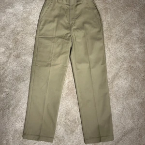 Dickies - Snygga beige byxor från Dickies med en klassisk design. De har en rak passform och är tillverkade i ett slitstarkt material. Perfekta för en stilren look. Byxorna har dragkedja och knapp framtill.